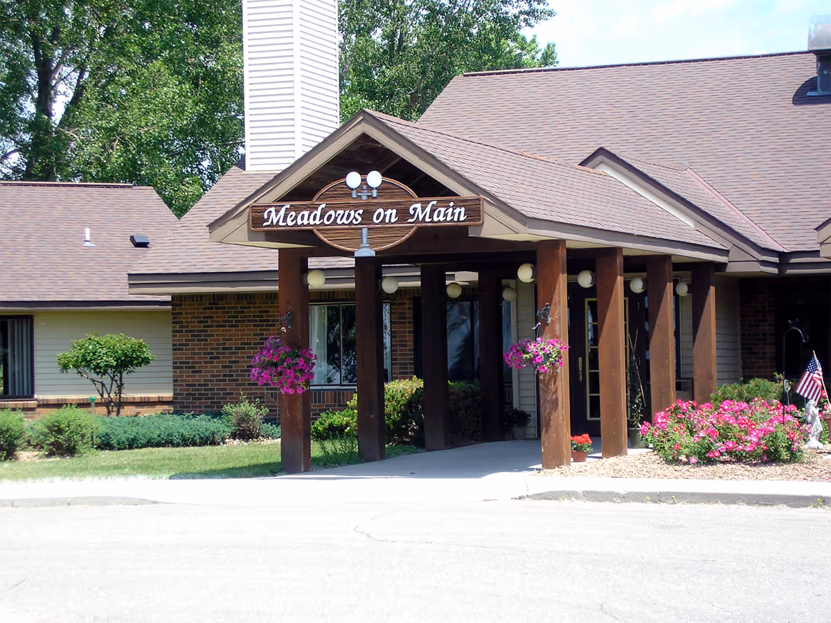 Front entrance of Meadows on Main senior living facility with wooden posts and hanging flower baskets