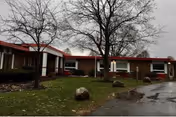 Exterior view of a single-story red-brick facility with bare trees and wet parking lot.