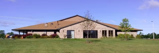 Single-story brick senior living facility with a grassy lawn and trees in front.