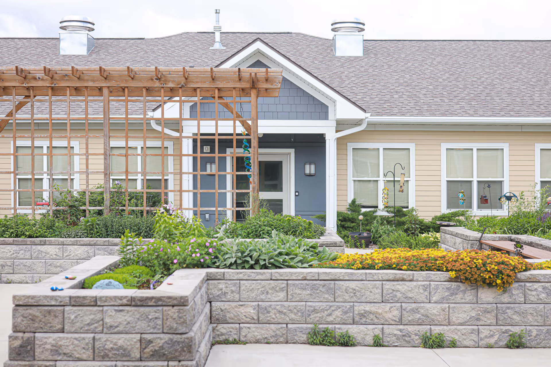 Exterior view of Rock Creek Senior Living with a wooden pergola and landscaped raised beds.