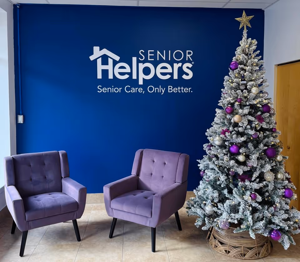 Lobby seating area with blue wall branding, two purple chairs, and a frosted Christmas tree.