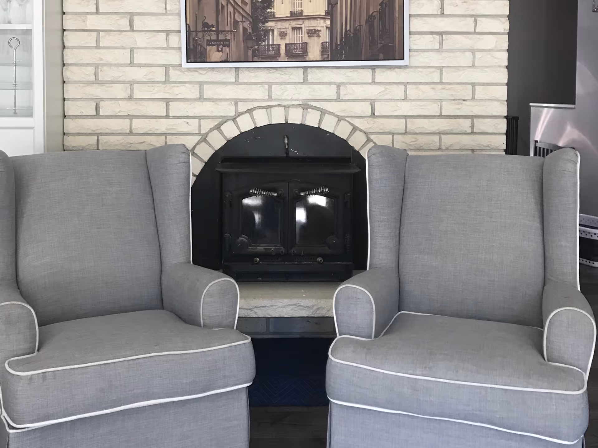 Two gray upholstered armchairs sit in front of a brick fireplace in a living room.