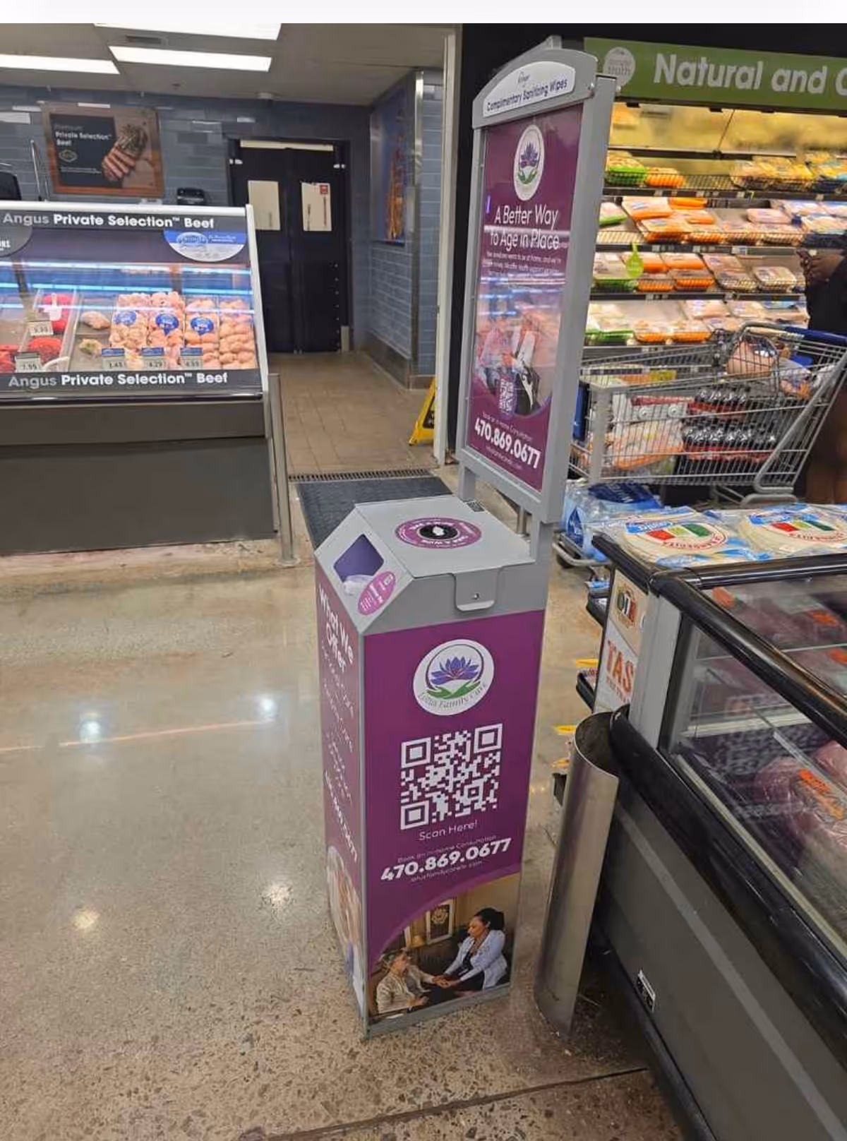 Purple promotional kiosk with QR code and Lotus Family Care signage in a grocery store.