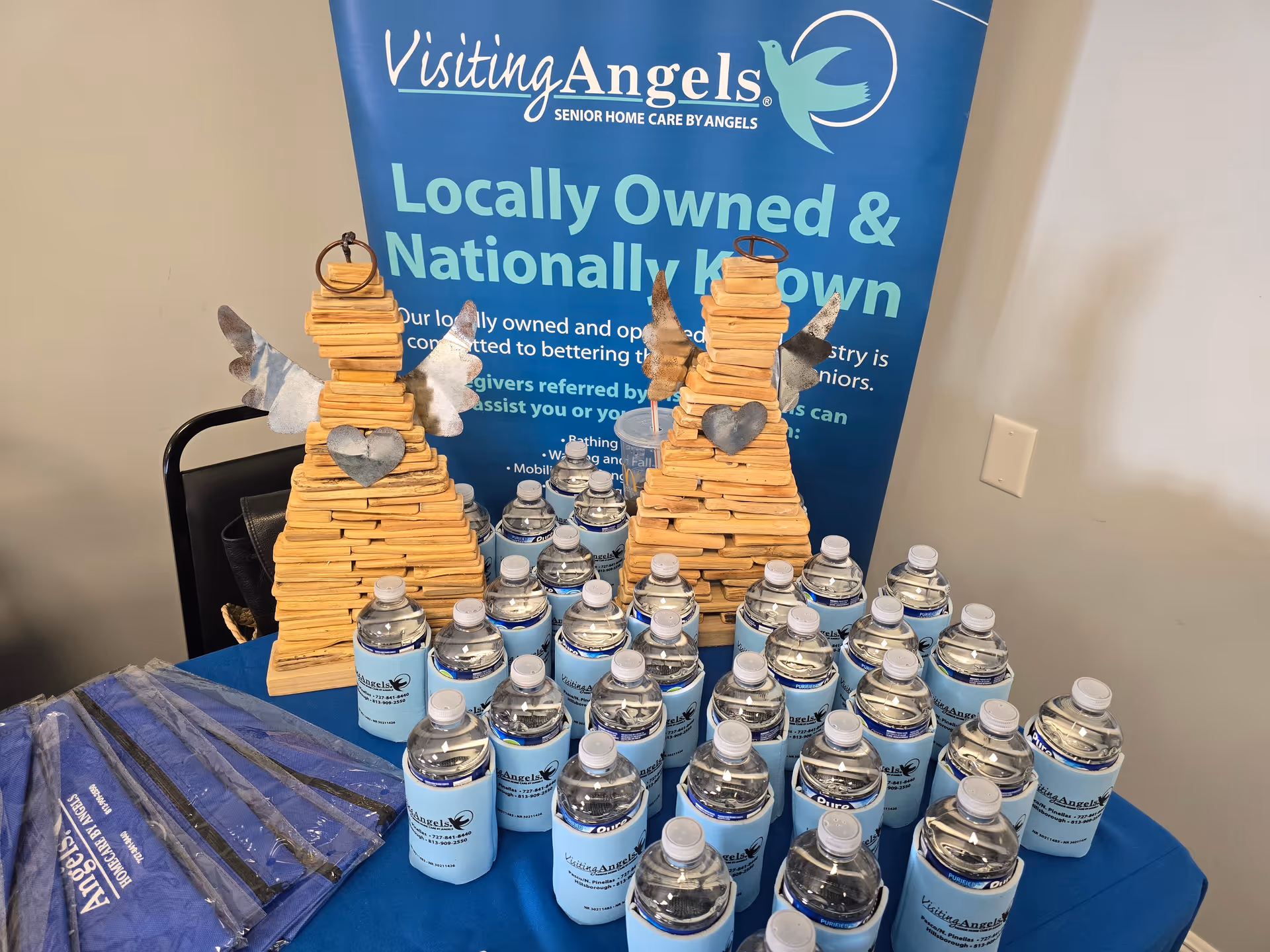 A table displays bottled water and wooden decorative angel sculptures in front of a banner.