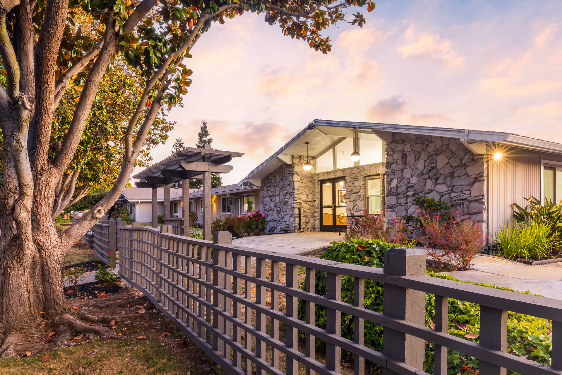 Sunset-lit exterior of a stone-clad senior living center with a wooden fence.