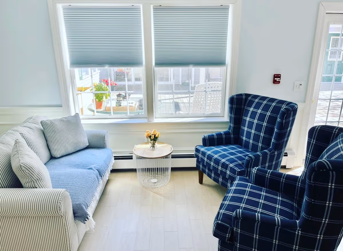 Bright living room with striped sofa, plaid armchairs, and a round glass-topped table by windows.
