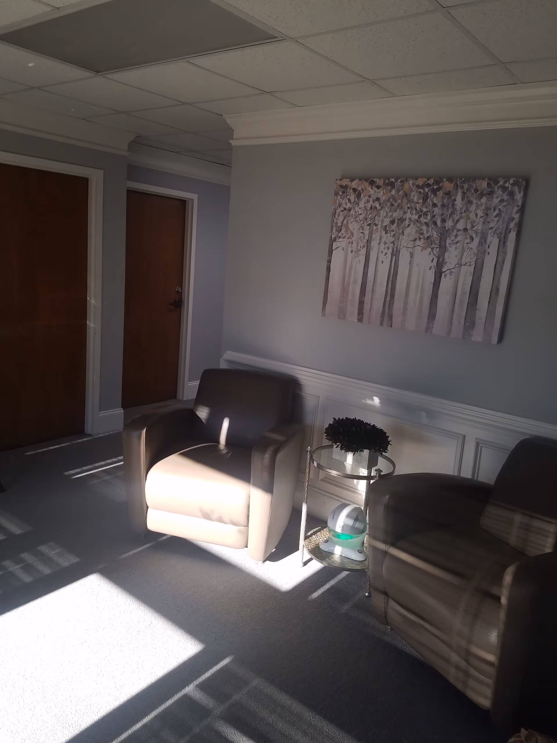 Two beige armchairs flank a glass side table in a quiet interior lounge.