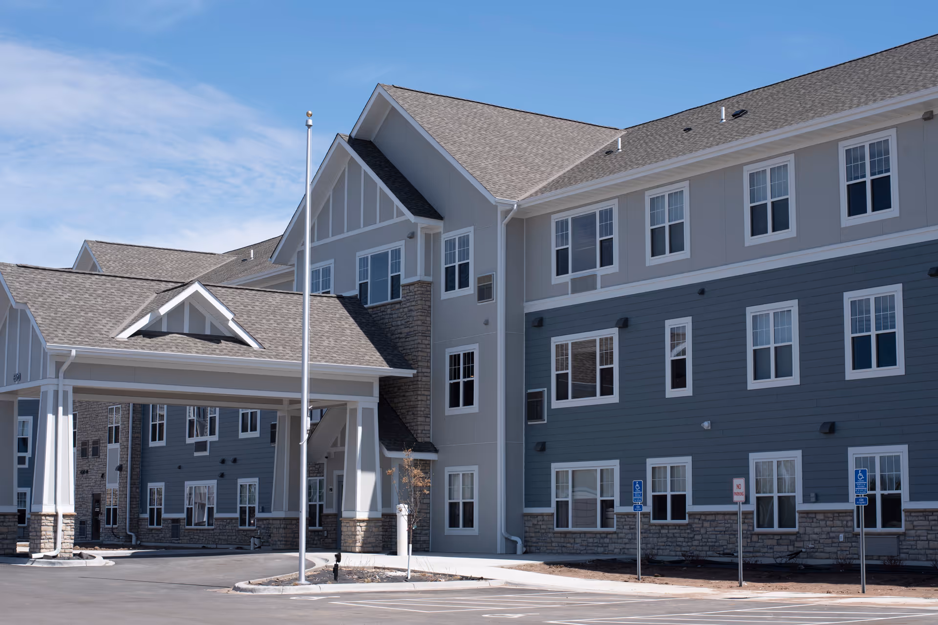 Modern multi-story senior living facility exterior with gray siding and stone accents.