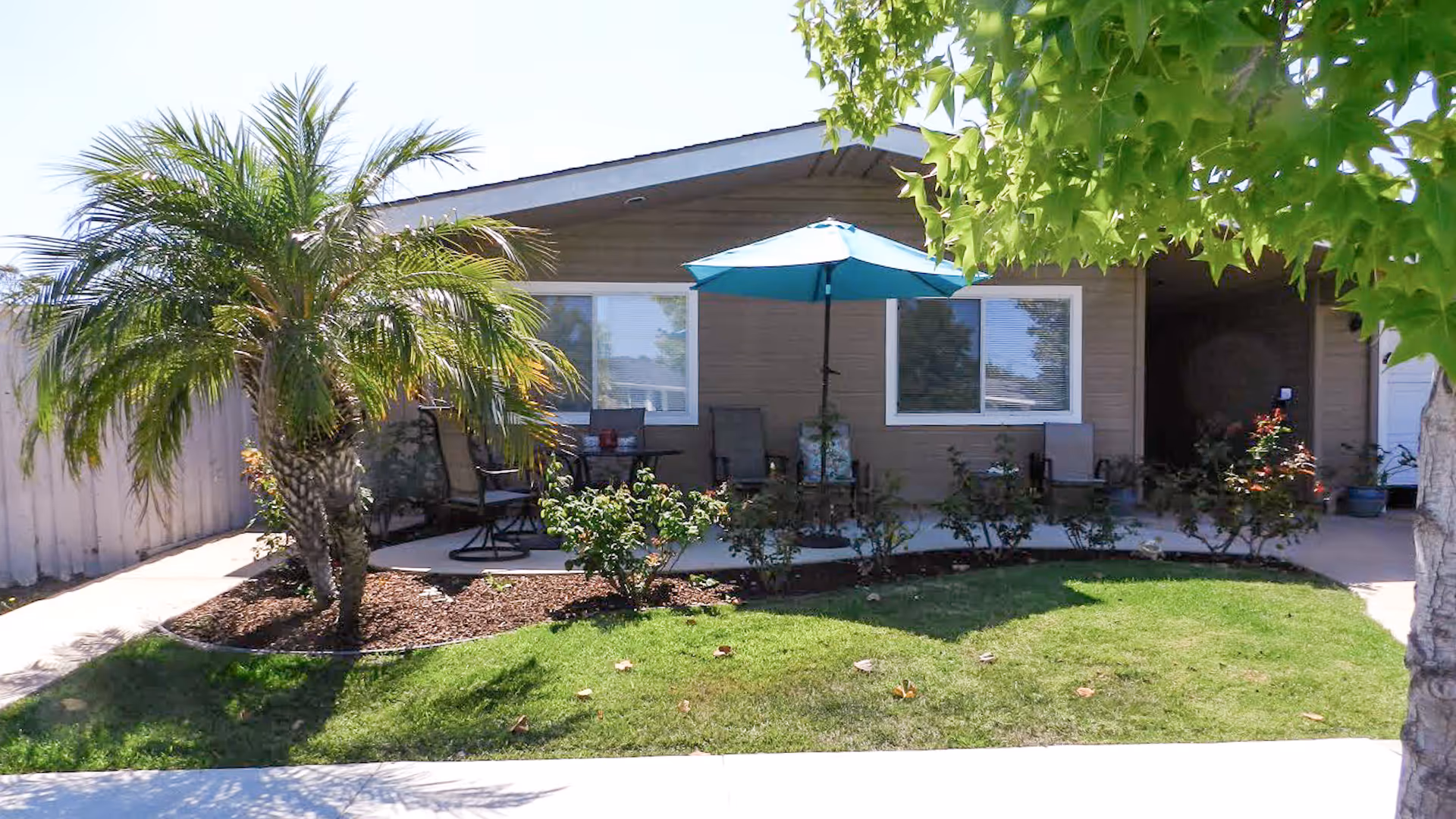 Single-story residential unit with a front patio, lawn, palm tree and a blue patio umbrella.