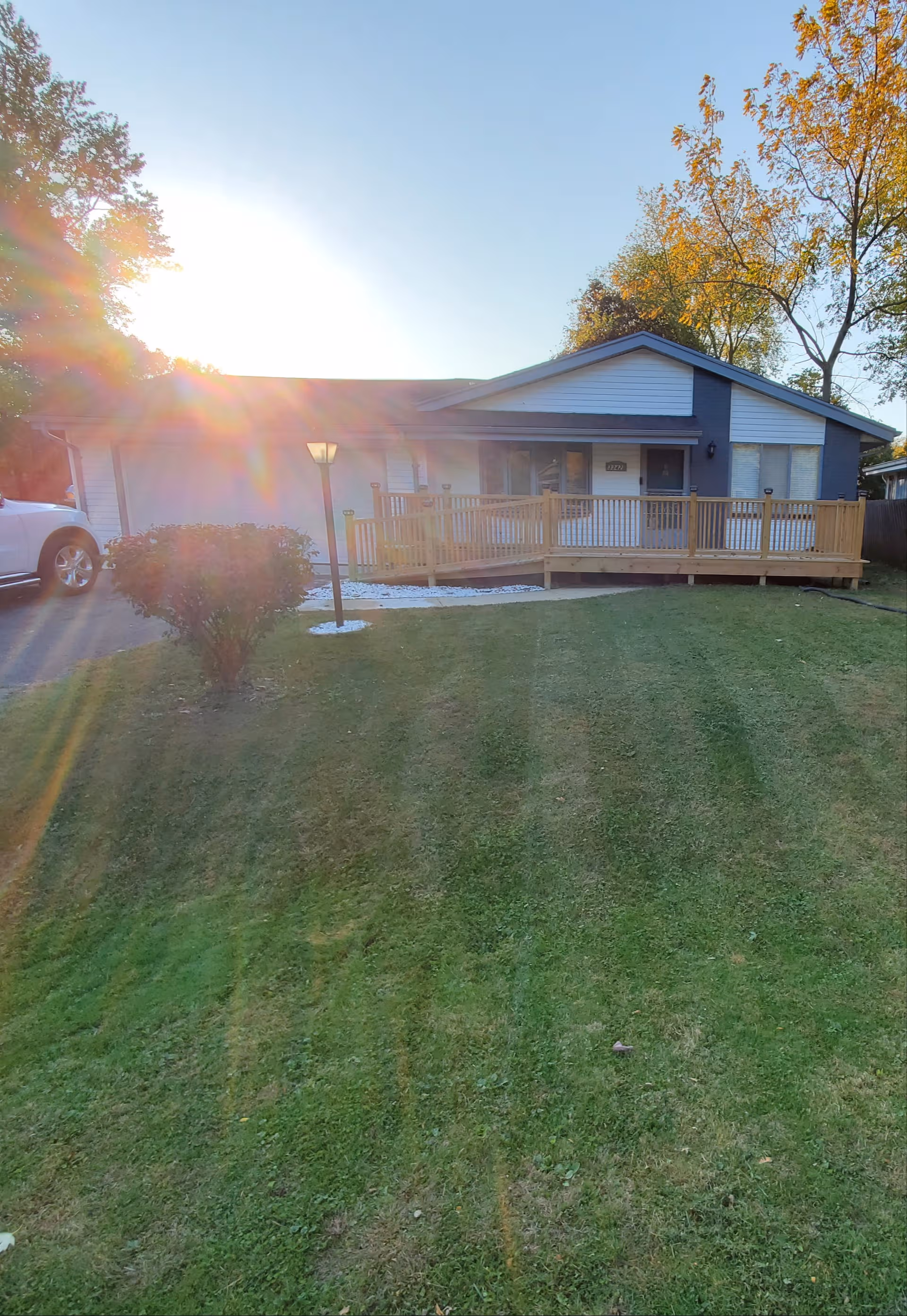 Front view of a single-story facility with a wooden ramp, lawn, and sun glare.