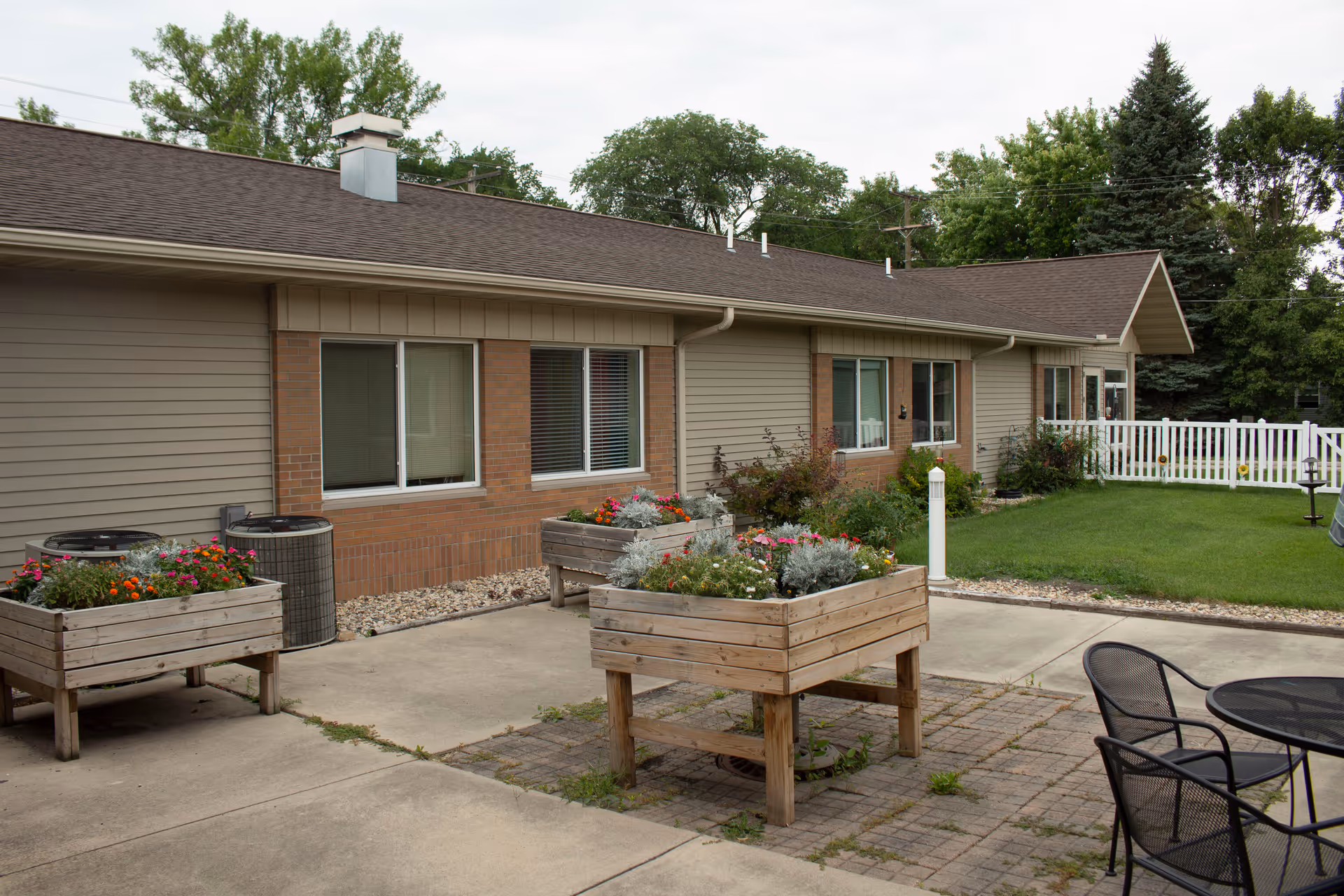 Exterior view of a senior living facility with wooden planters, patio furniture, and a lawn.