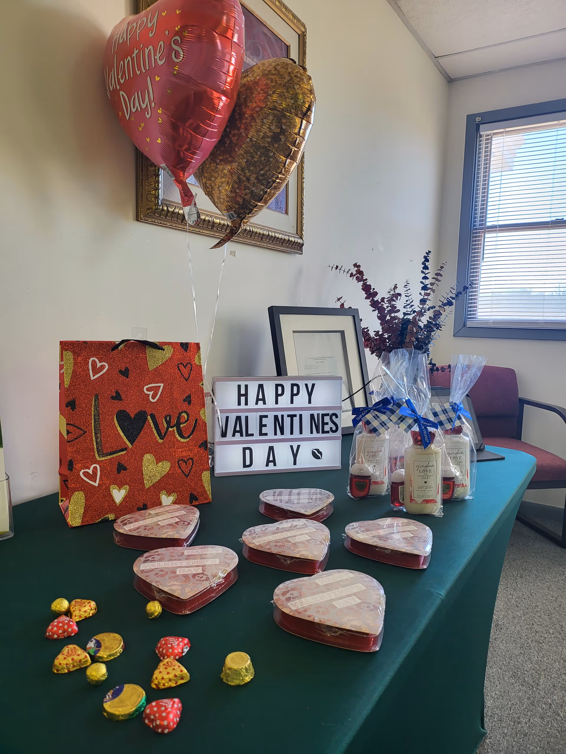 Valentine's Day display on a table with a sign, balloons, gifts, and heart-shaped tins.