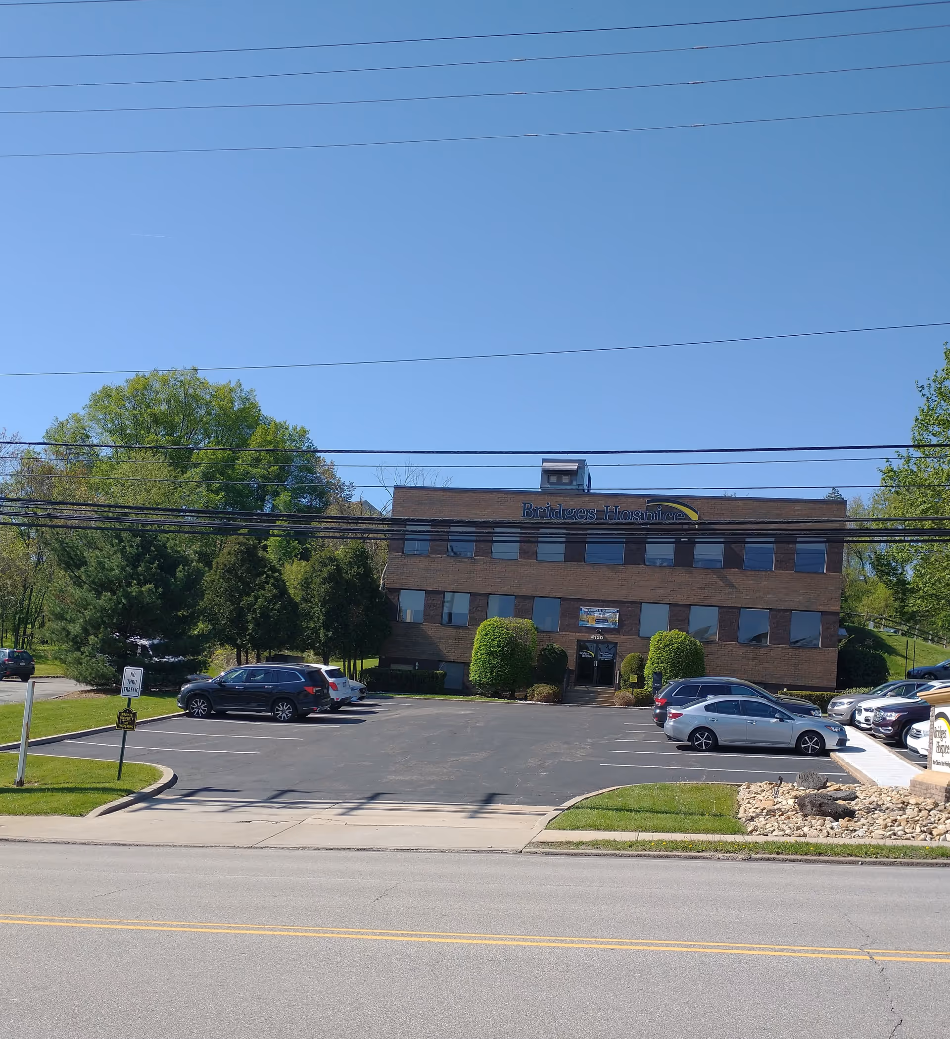 Exterior view of Bridges Hospice brick building with parked cars and clear blue sky.