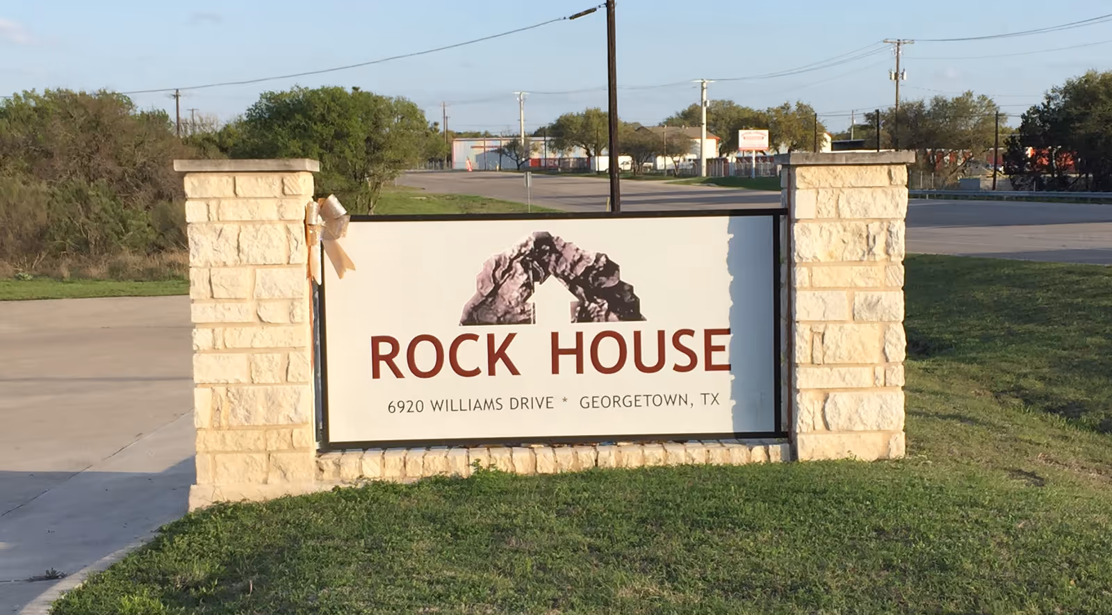 Stone entrance sign for Rock House with address along a grassy roadside.
