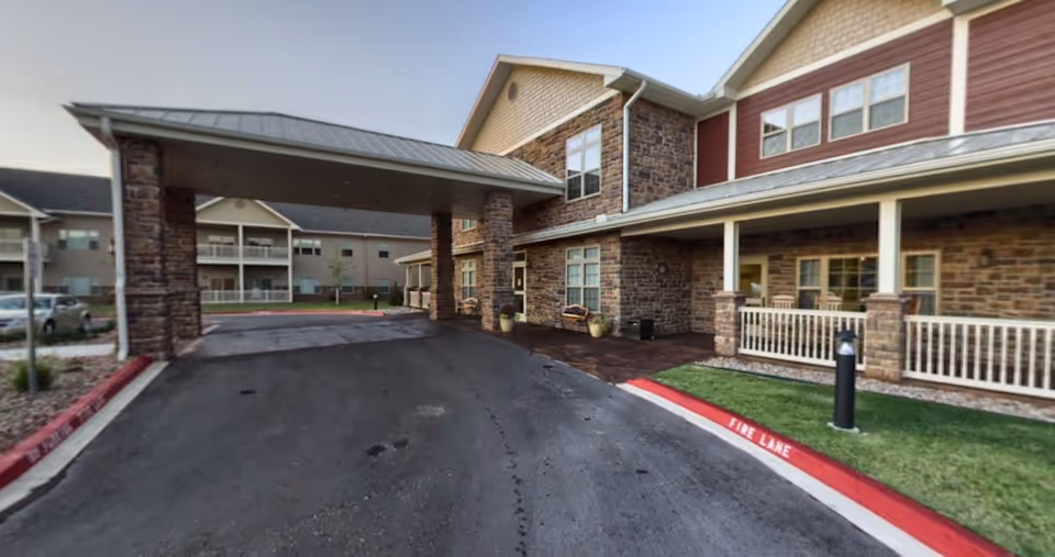Covered porte-cochere and front entrance of a stone-clad retirement community building with a driveway and curb marked FIRE LANE.