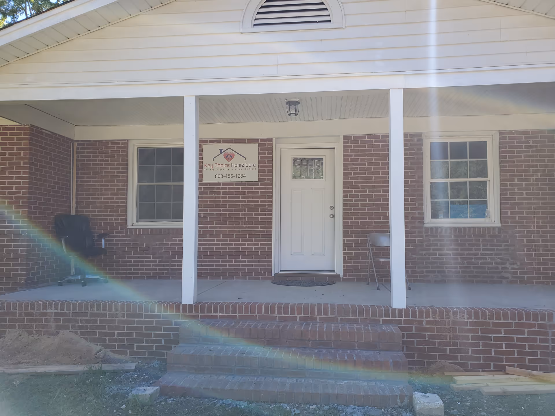 Brick senior care facility entrance with white door and windows under a porch.