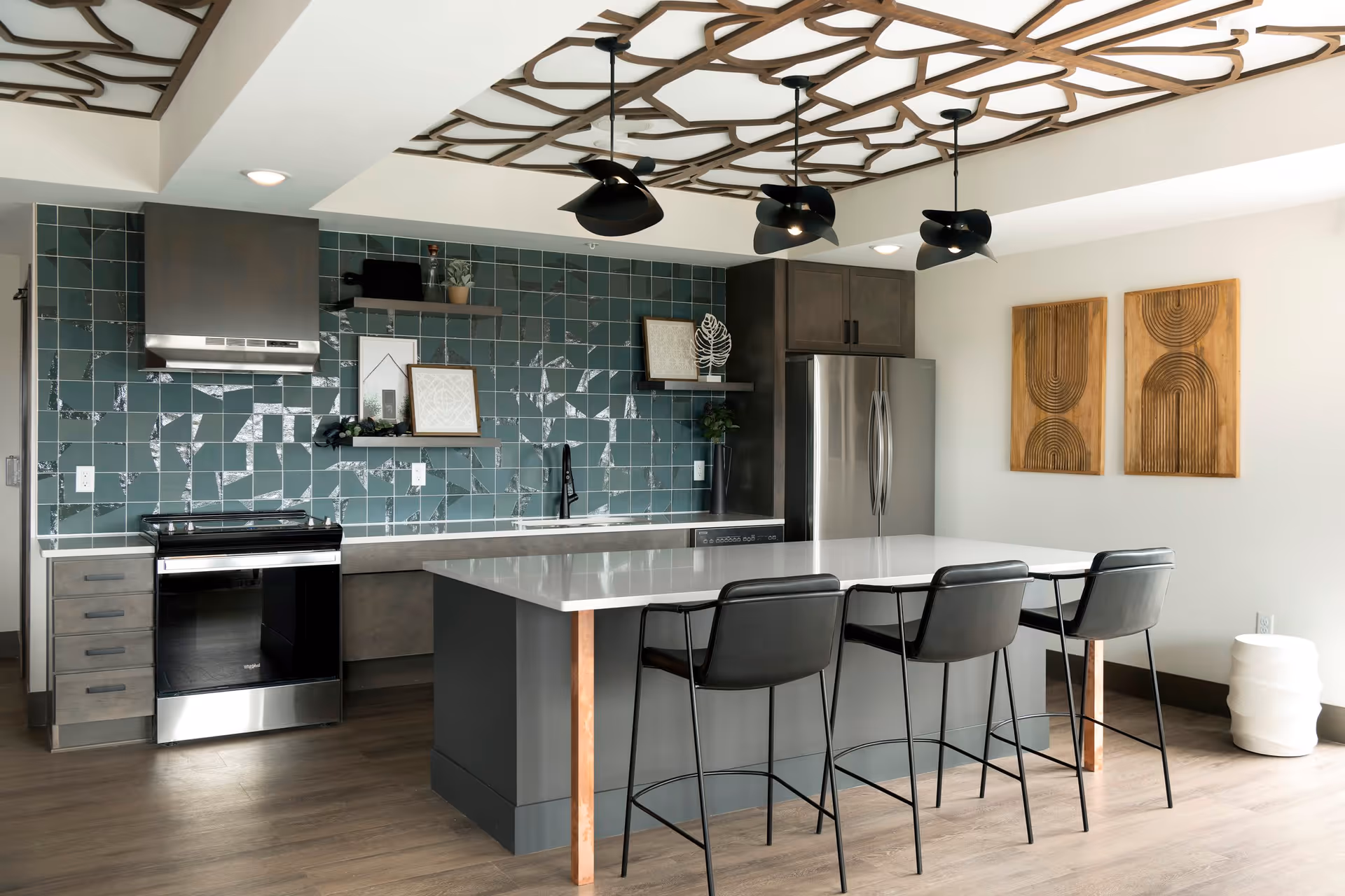 Modern kitchen with a large island, four bar stools, stainless steel appliances, and a decorative green tile backsplash.