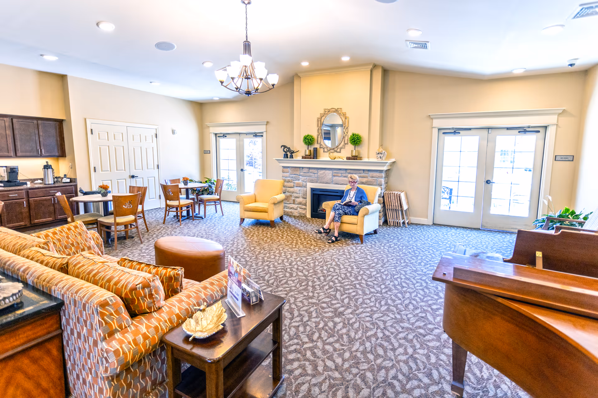 Lounge in Oak Pointe of Monett with fireplace, seating clusters, and a resident seated.