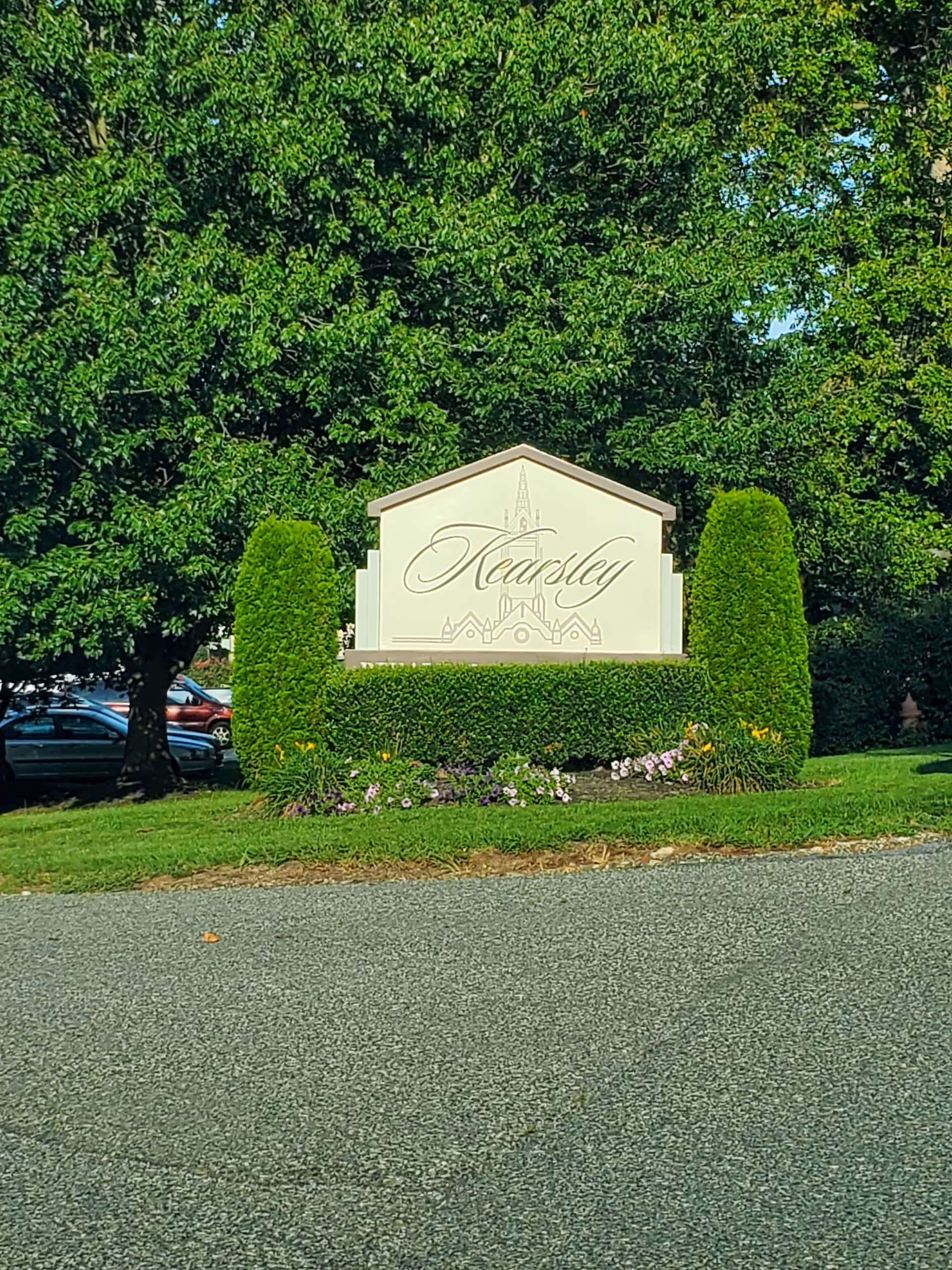 Sign reading 'Kearsley' with hedges and flowers at the facility's exterior entrance