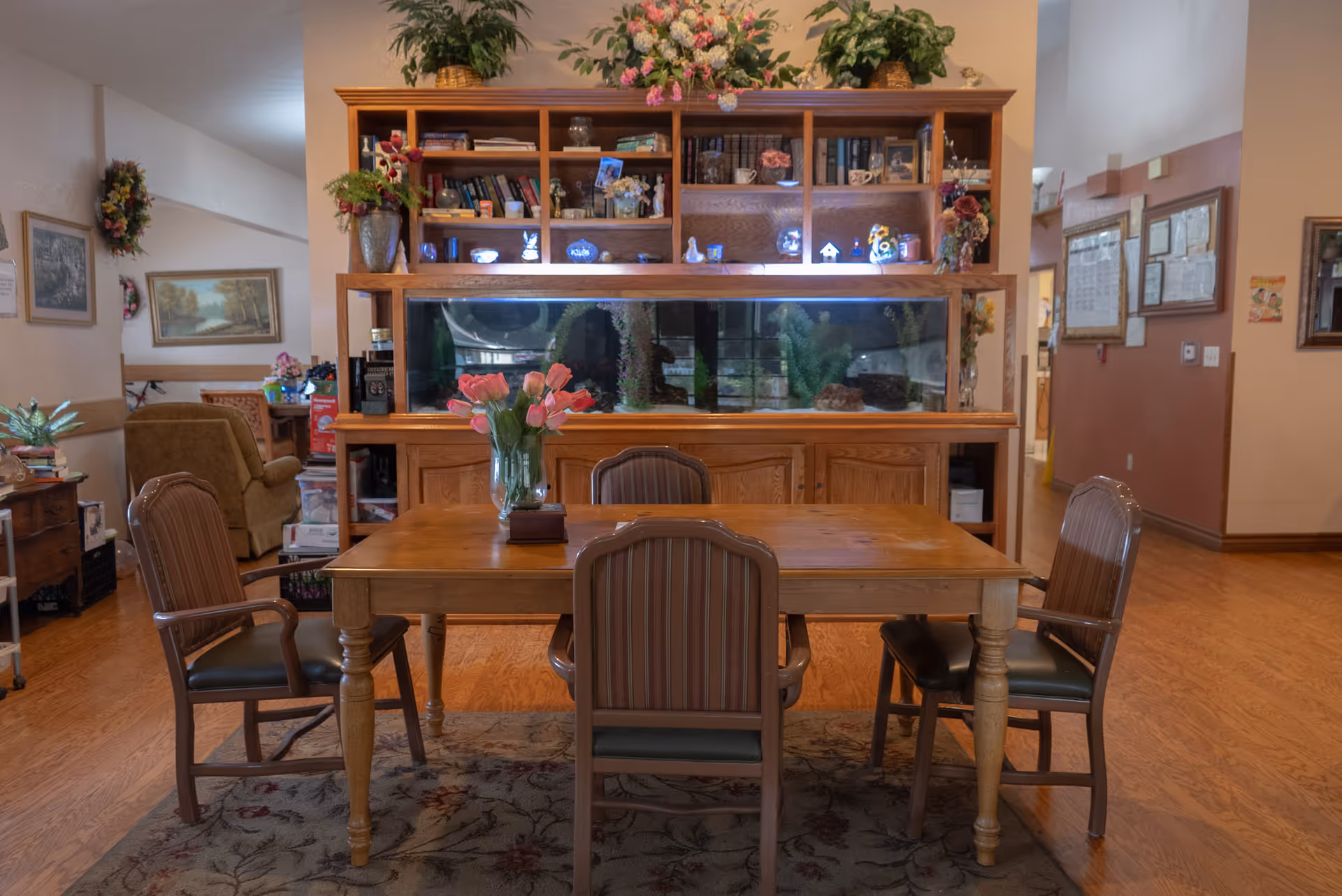 Wooden dining table with five chairs in a cozy common room, near an aquarium.