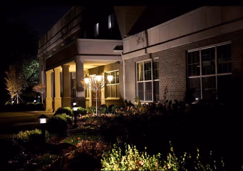 Night view of a brick building's front entrance with columns, lit pathway lights, and landscaped beds.