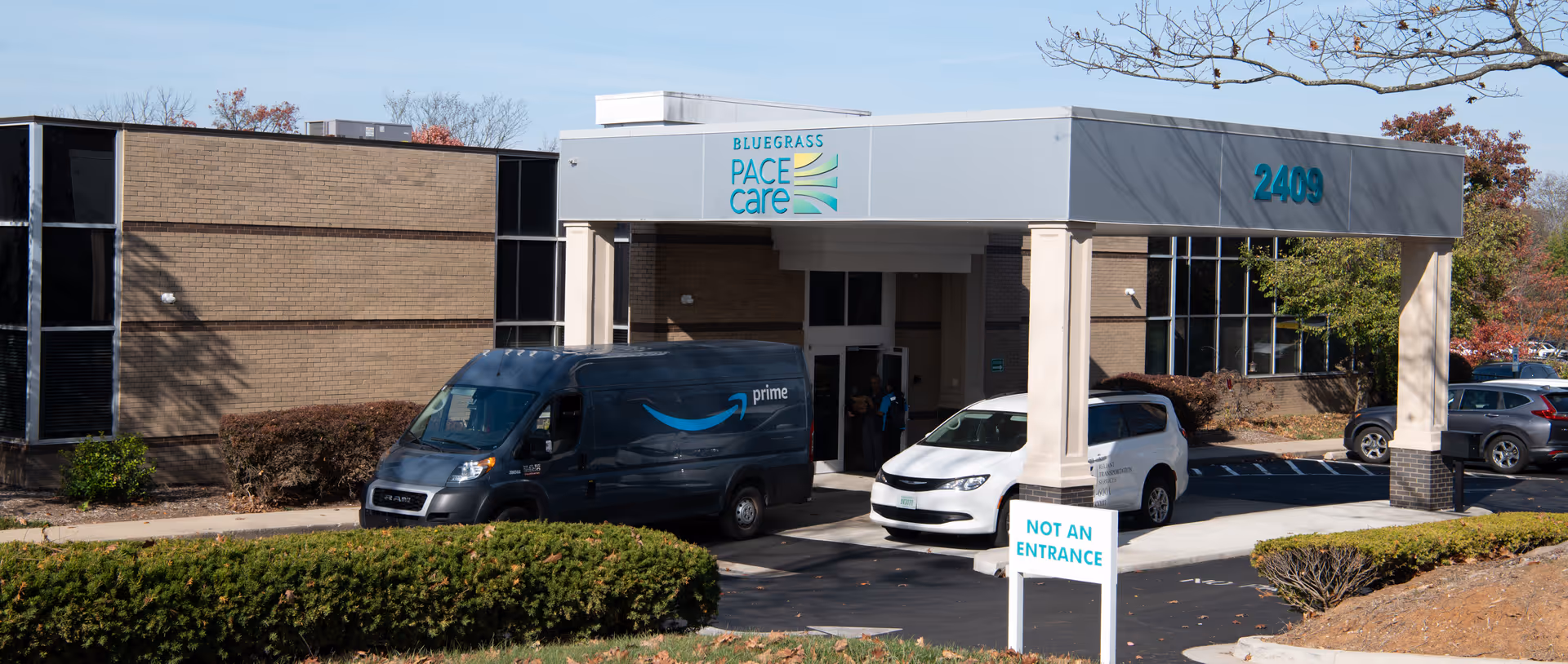 Exterior view of Bluegrass PACE Care facility entrance with parked vans.