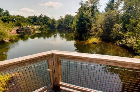Wooden railing overlooks a calm lake framed by trees.