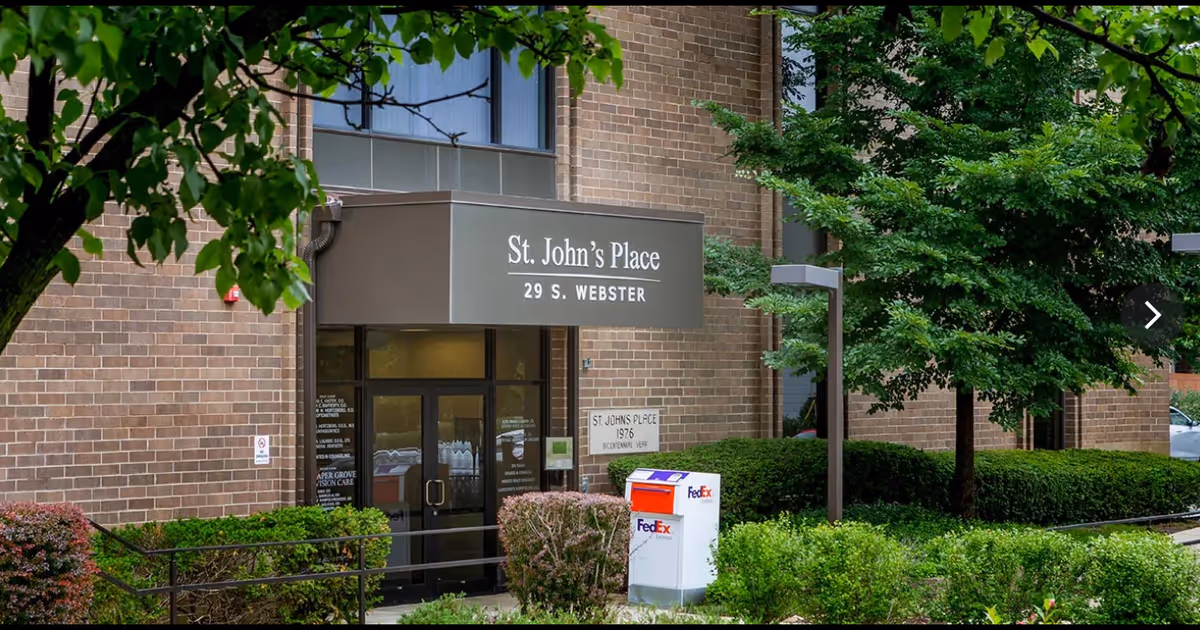Brick building entrance with St. John's Place sign, glass doors, and greenery.