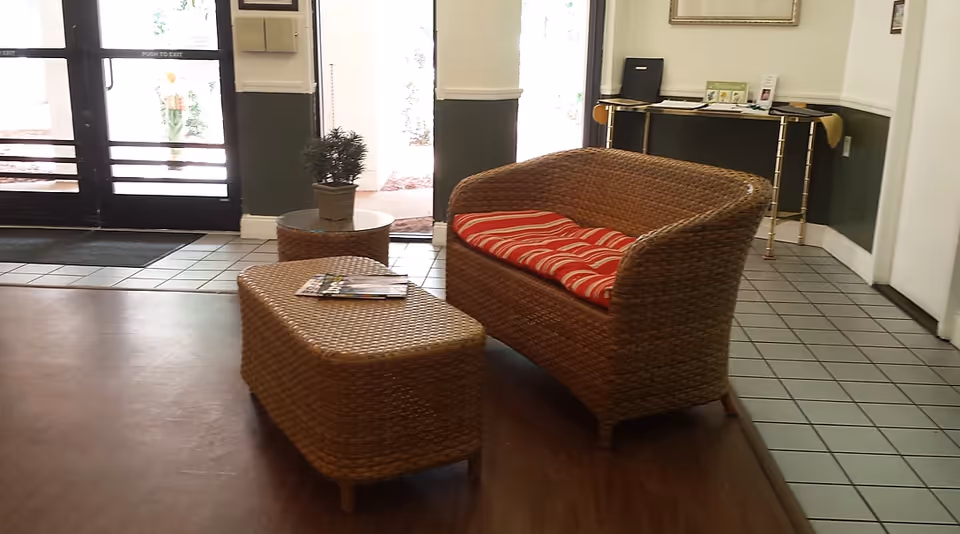 Wicker loveseat and ottoman with red cushions in a lobby-style interior near glass doors.