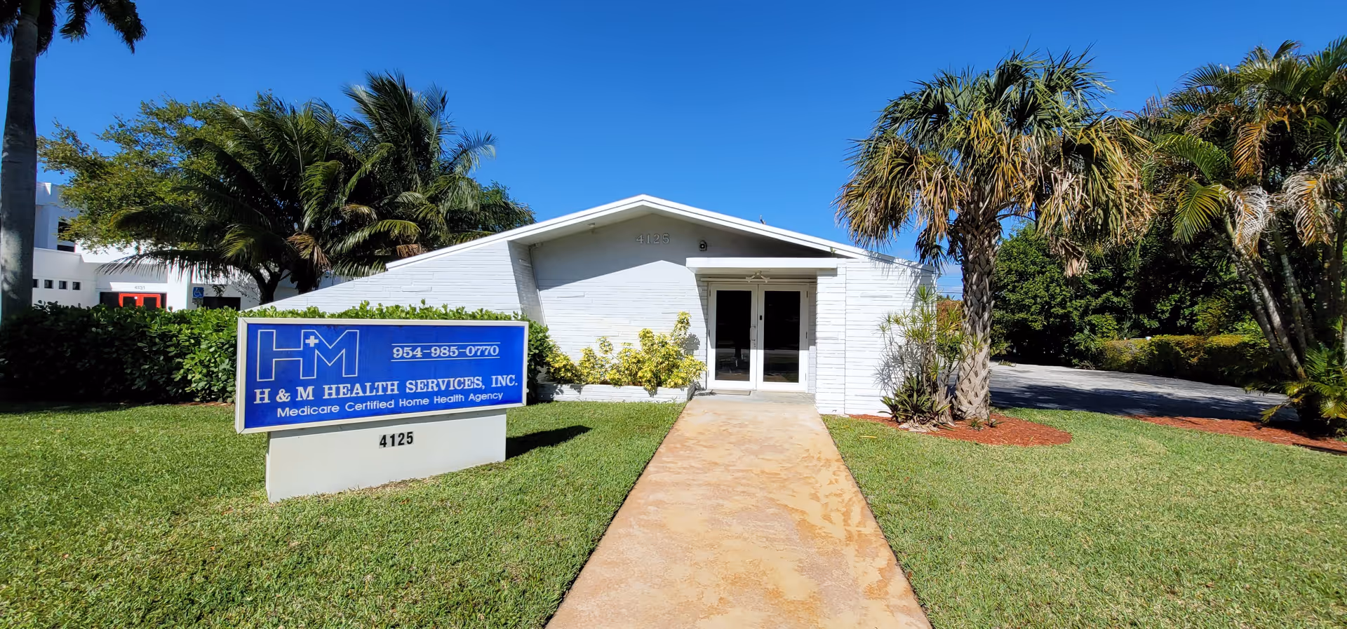 Front view of a white single-story building with a blue H&M Health Services sign.