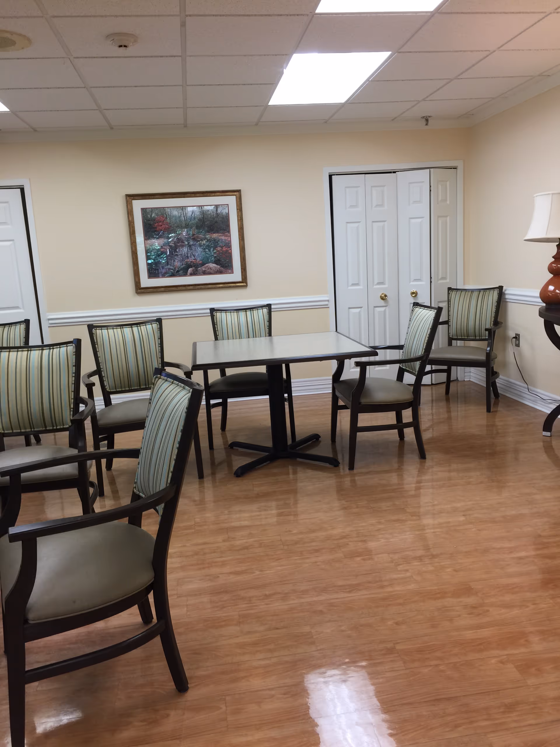 Interior of a senior living dining room with a central table and striped armchairs.