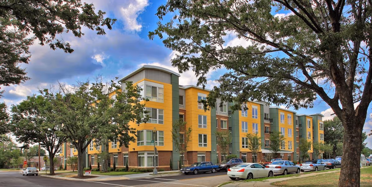 Front exterior of Victory Square Apartments, a colorful four-story senior living building with parked cars.