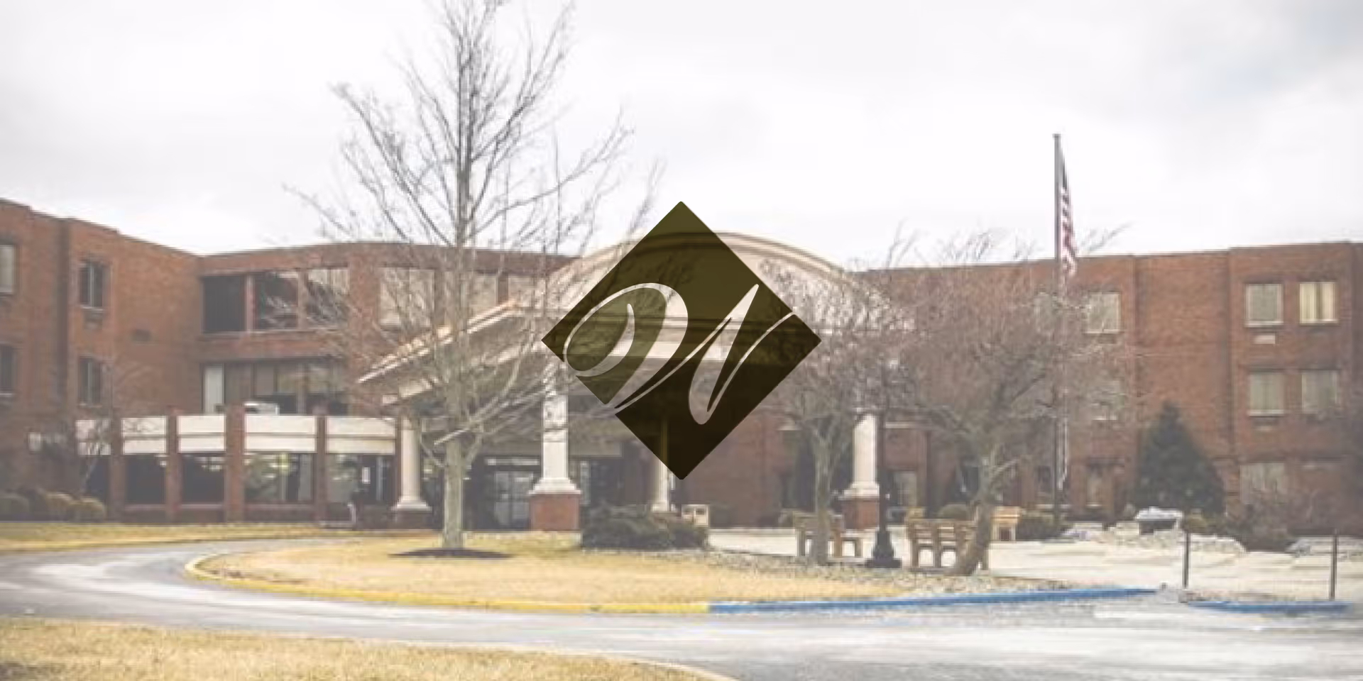 Brick senior living facility exterior with circular driveway and bare trees.