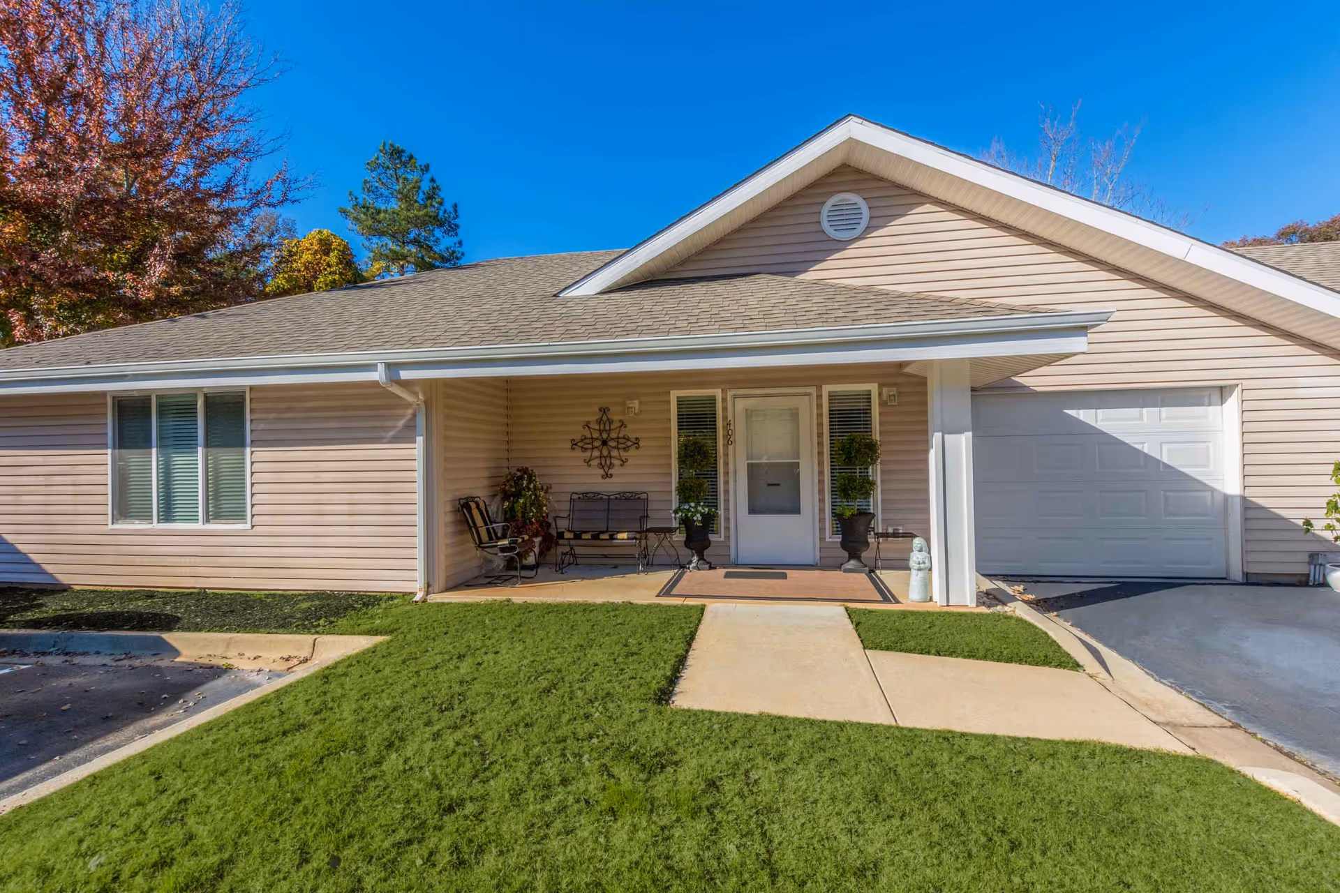 Single-story residence front with a covered porch, entrance door, attached garage, and a green lawn.