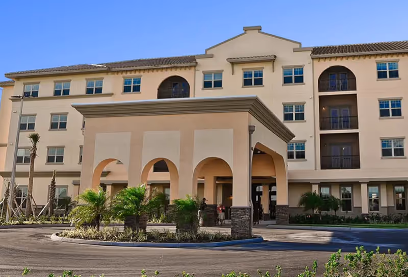 Exterior view of a Mediterranean-style senior living campus with a porte-cochère and palm landscaping.