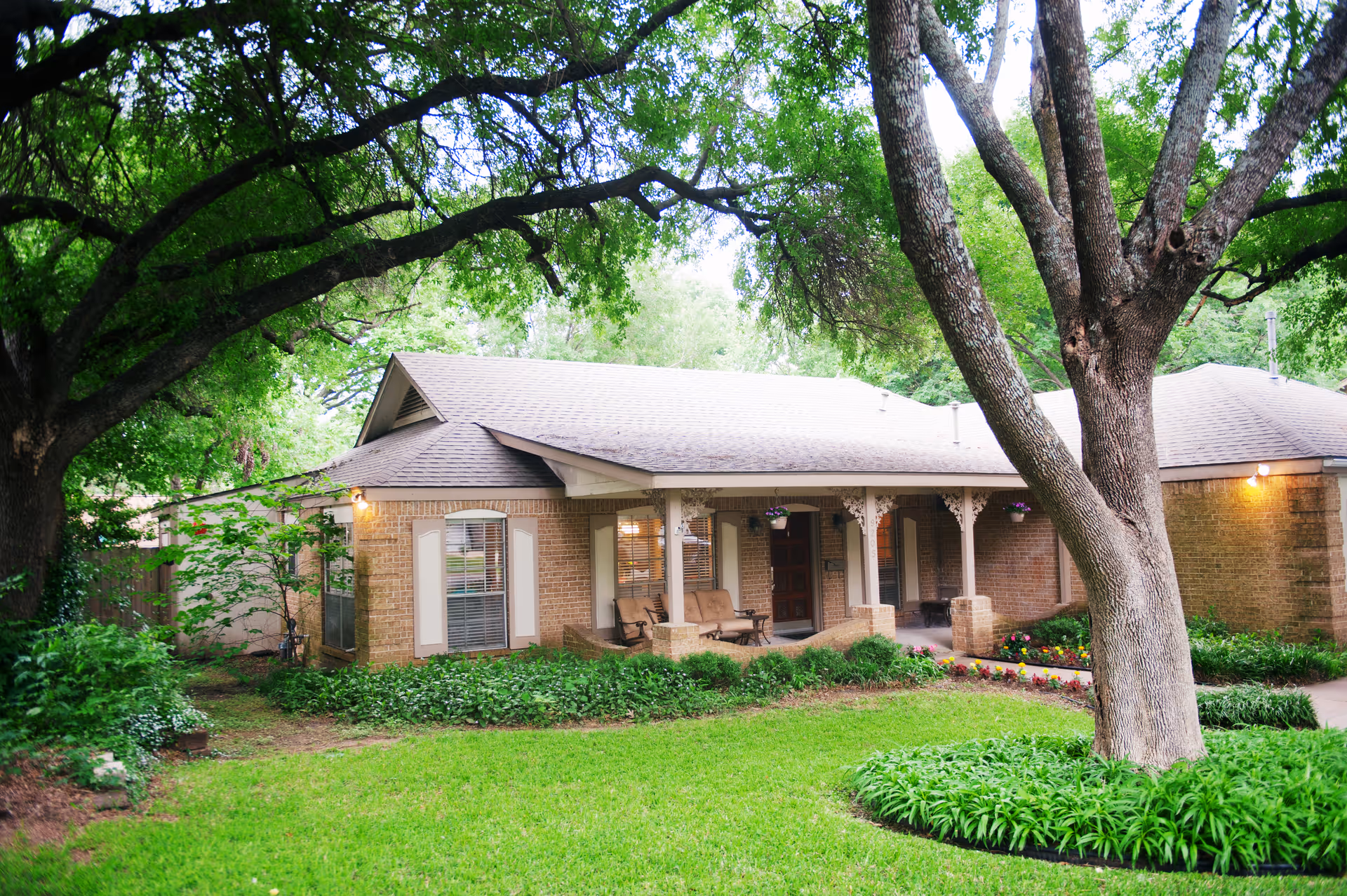 Front view of a brick senior living house with a shaded porch and manicured garden.