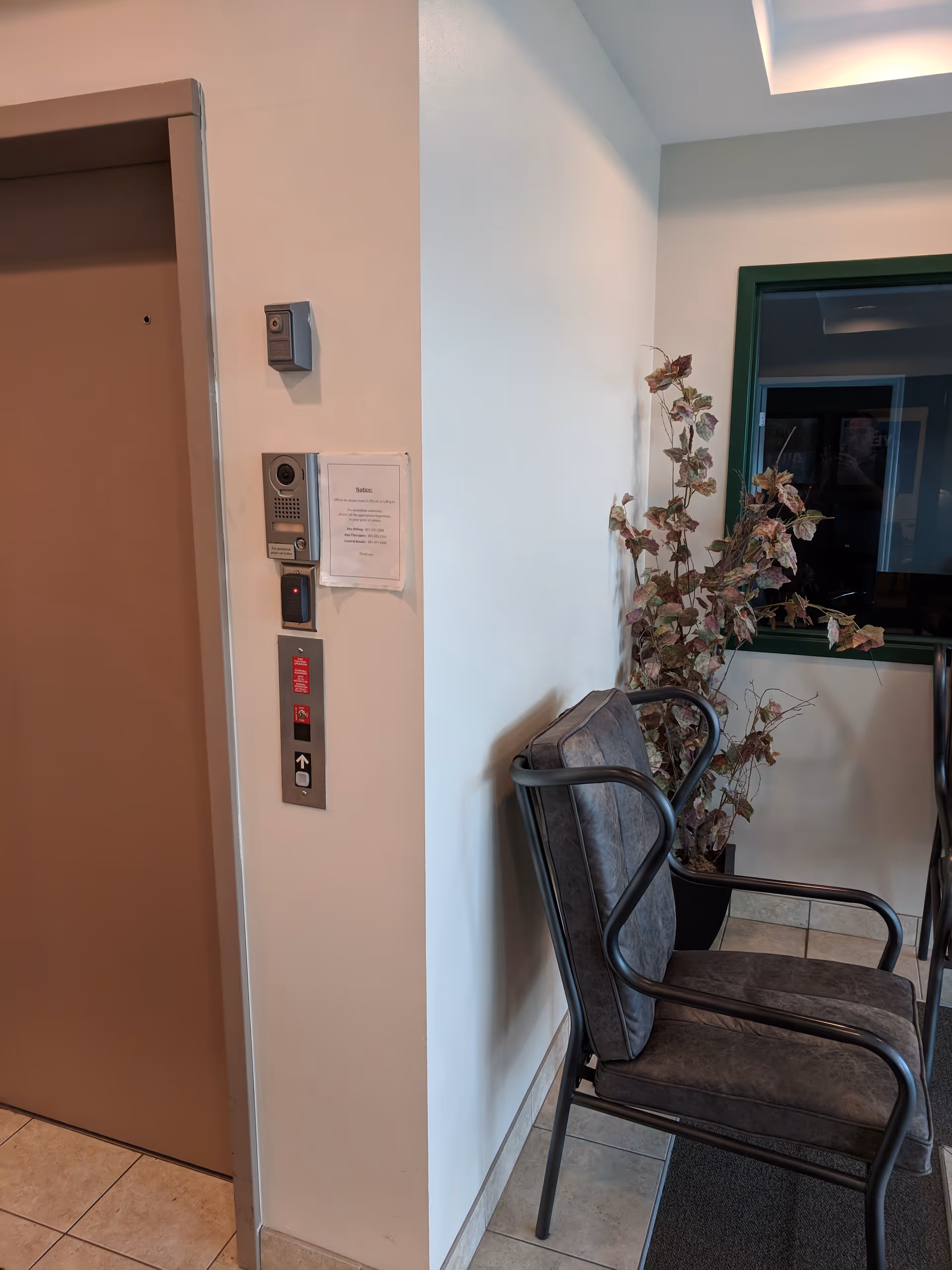 Elevator door on left, seating area with a potted plant in hallway