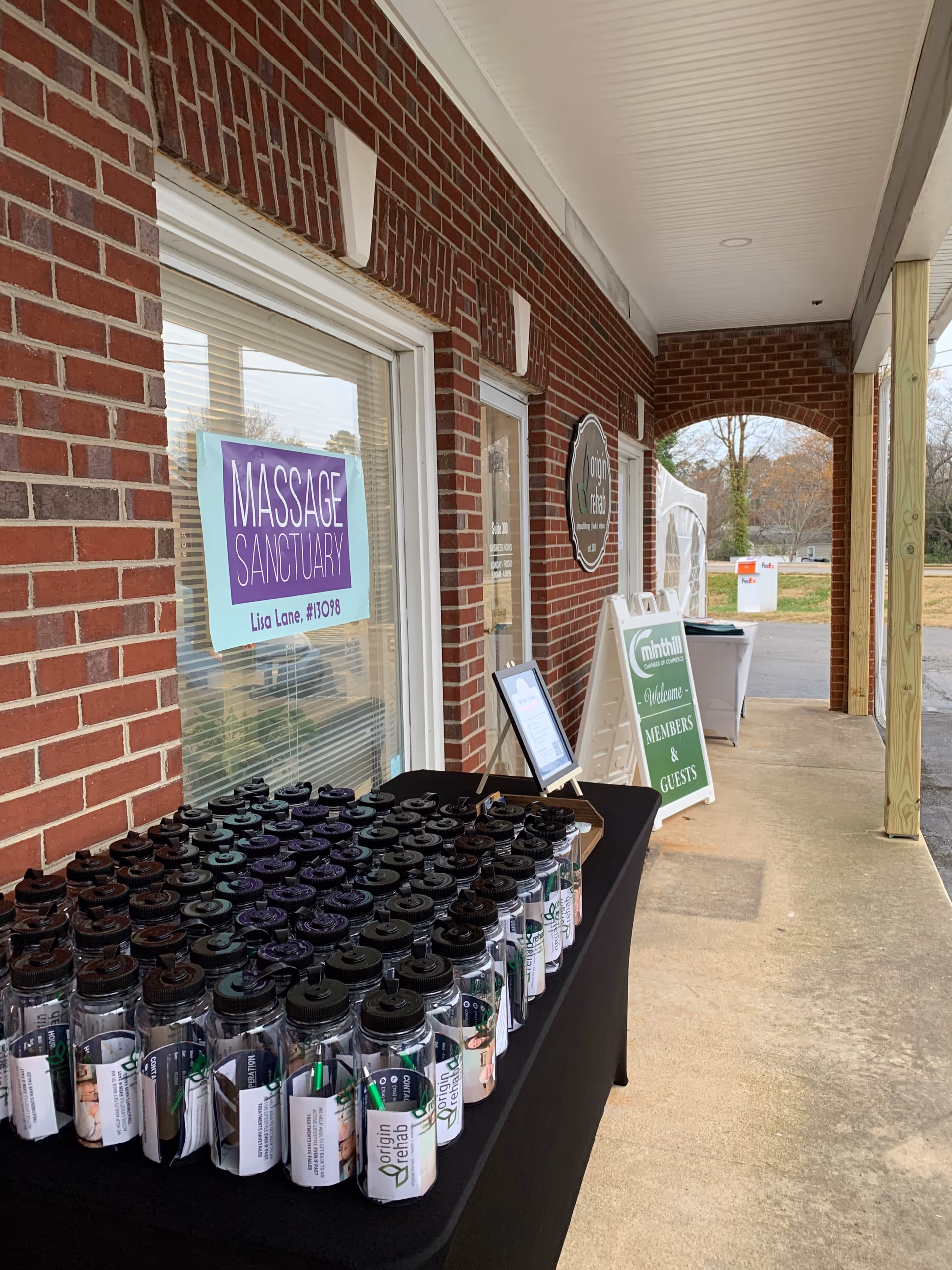 A brick facility exterior showing a table with water bottles and signs near a walkway.