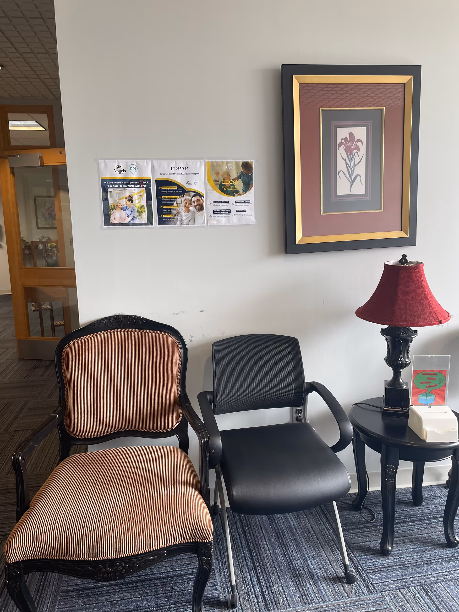 A small seating area with two chairs, a side table, lamp, and framed wall art.