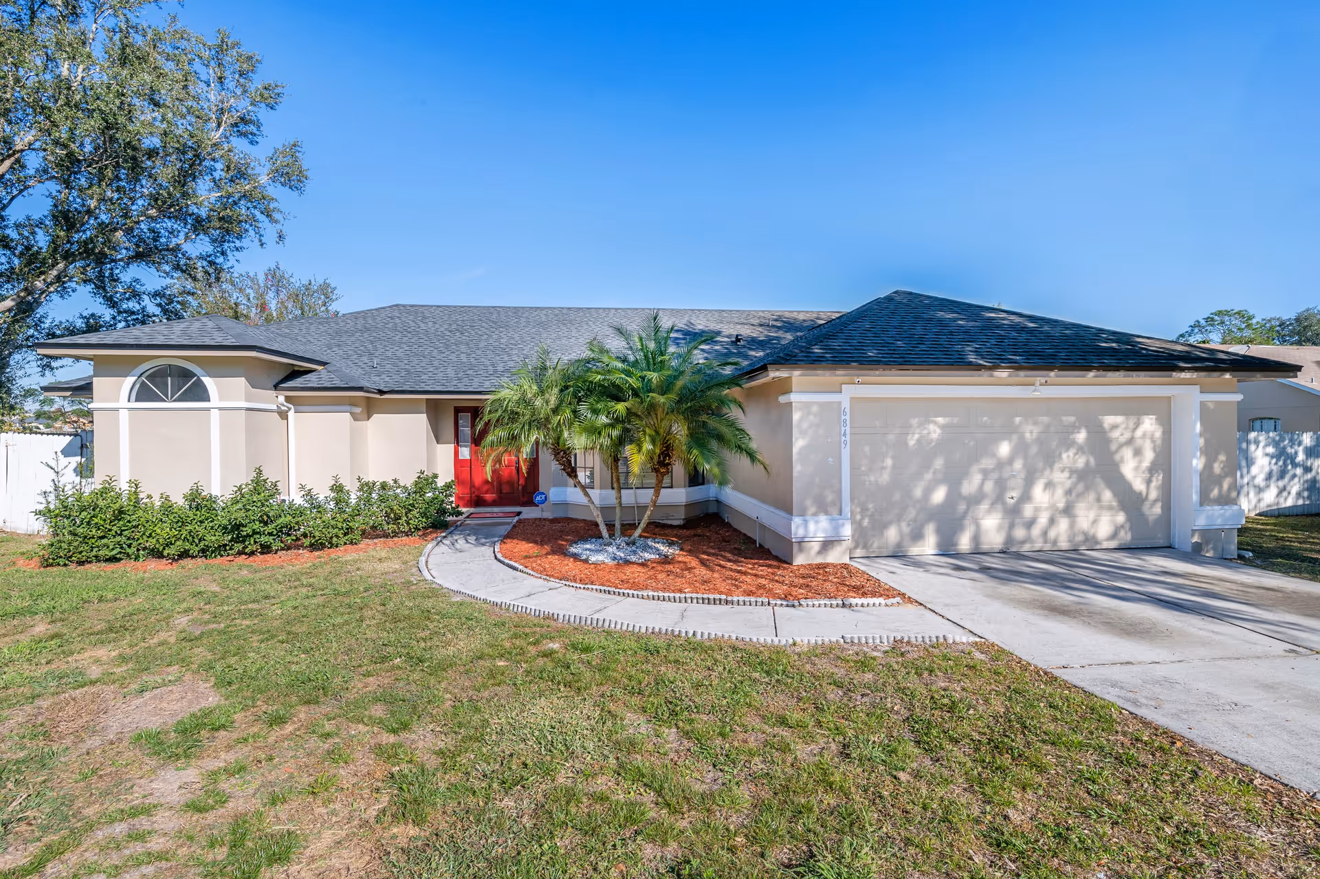 Single-story beige senior living home with a red front door, palm tree, and a two-car garage.