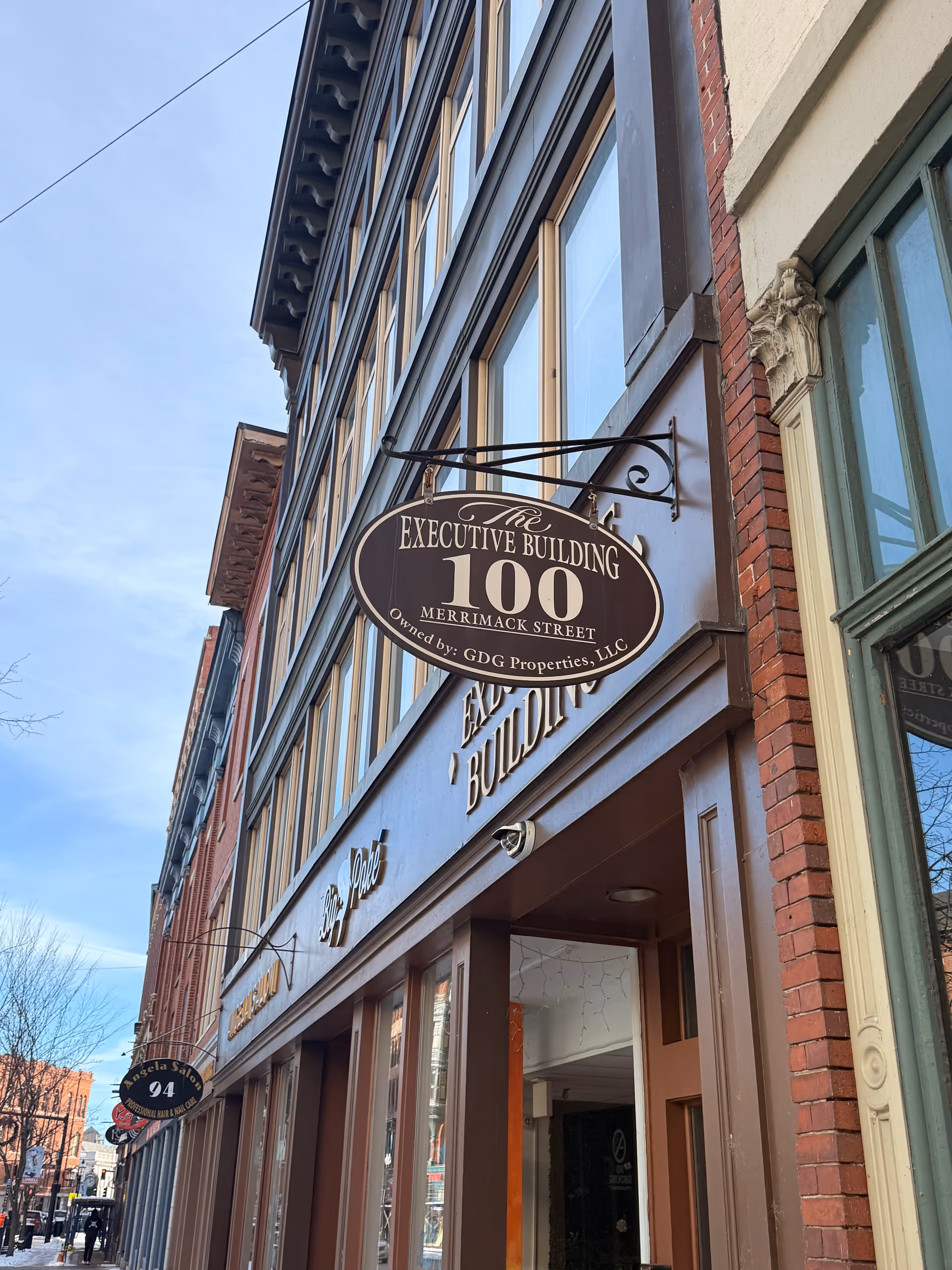 Street-level view of a brick building with a sign reading The Executive Building 100 Merrimack.