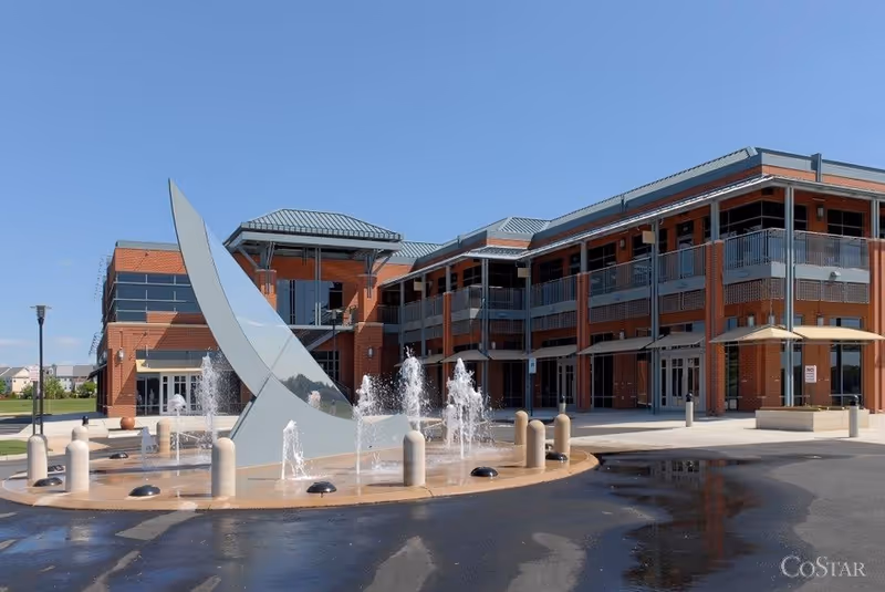 Modern brick senior living building with a circular fountain and outdoor seating area.
