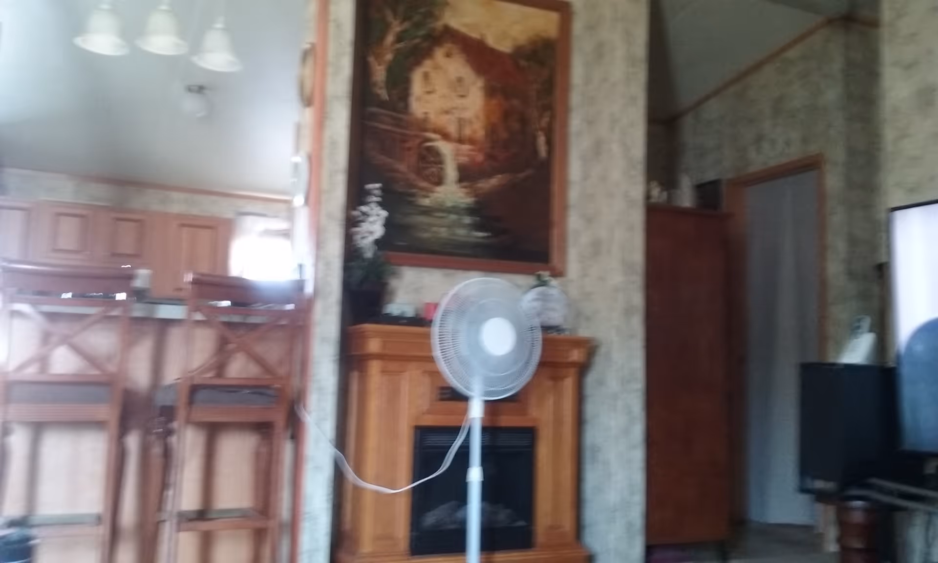 Living area with fireplace, wooden cabinets, bar stools, and a standing fan.