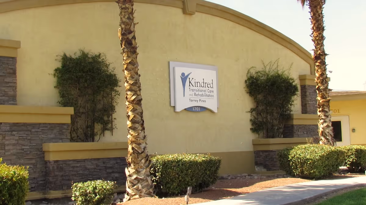 Exterior view of Torrey Pines facility with Kindred Transition Care sign and palm trees.