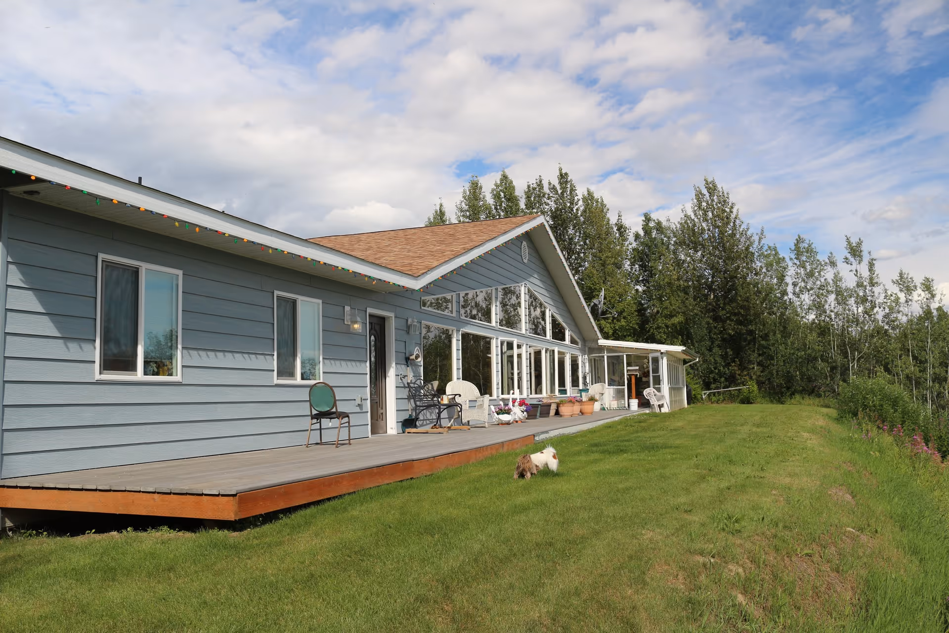 Blue single-story facility with a wooden deck, porch chairs, and a grassy, tree-lined lawn.