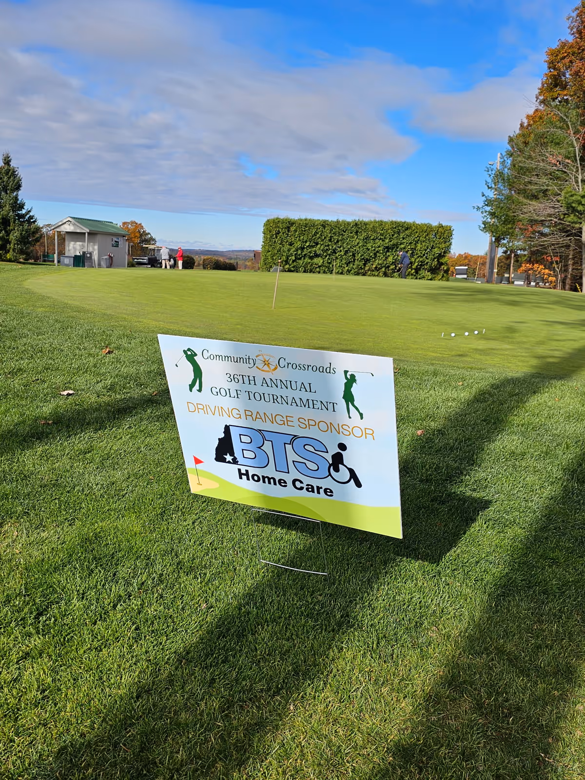 Bright green golf course with sponsor sign and distant people on a sunny day.