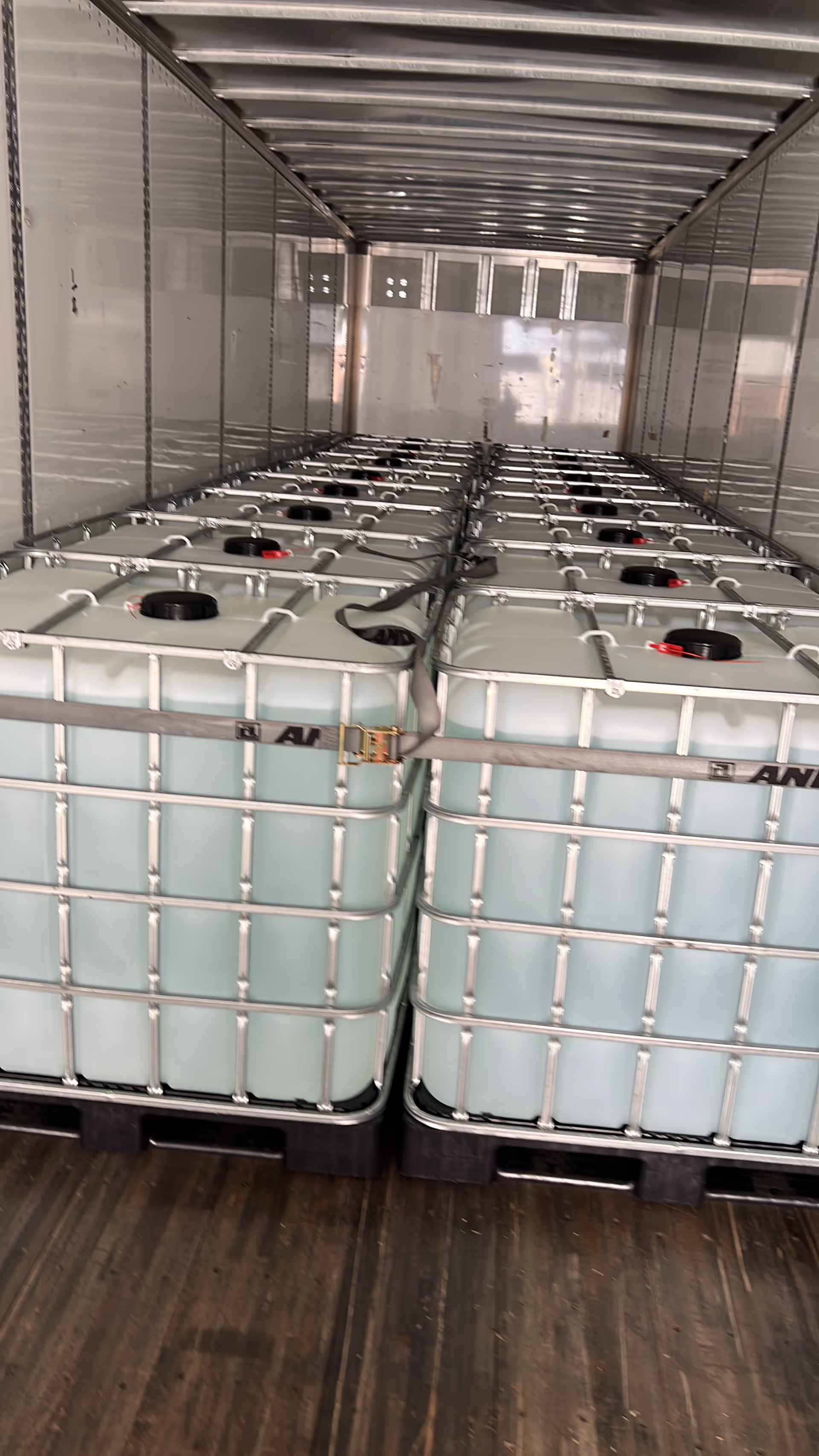 Inside a trailer, large IBC water tanks stacked in metal cages.
