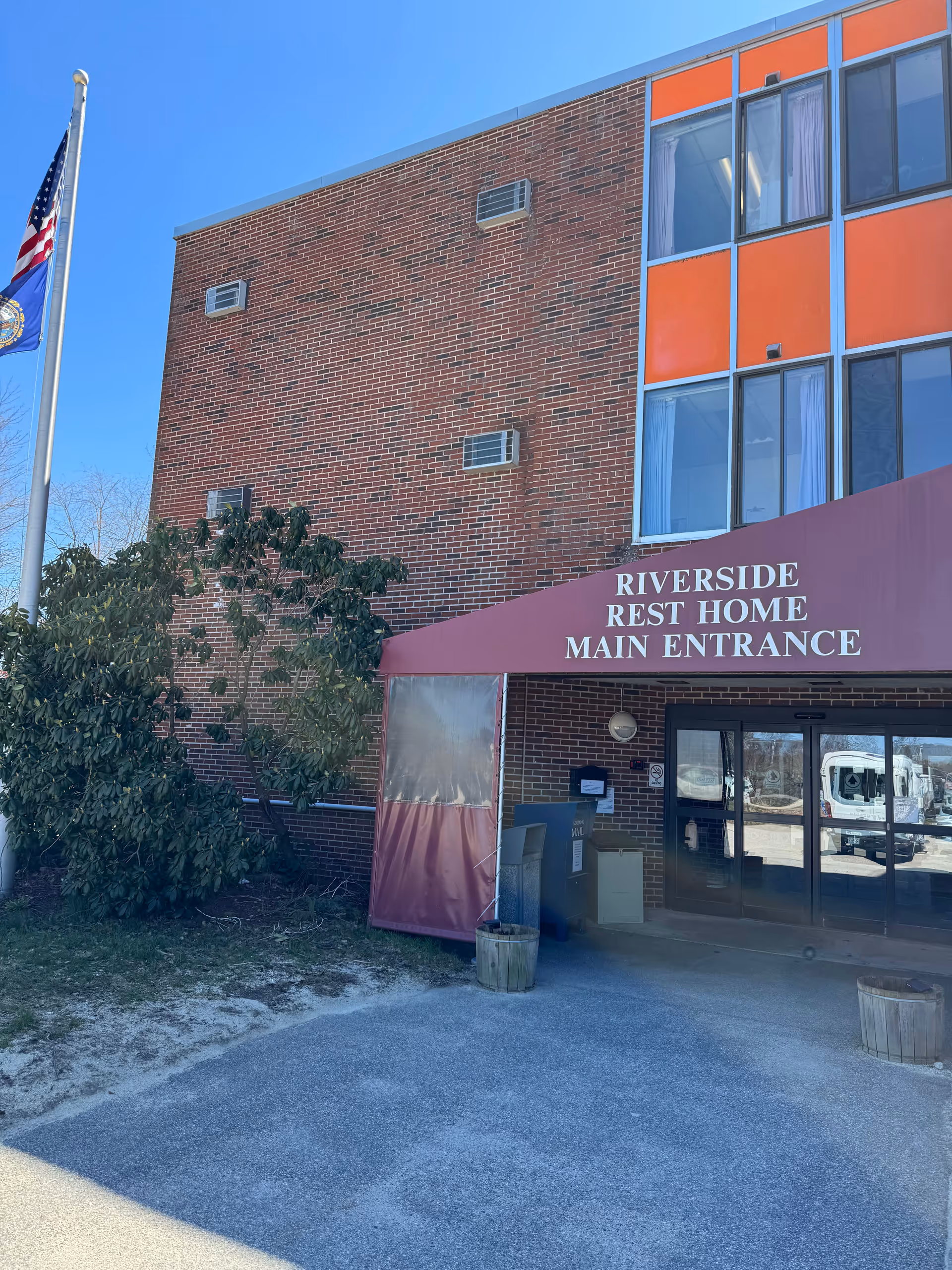 Brick senior care building with Riverside Rest Home main entrance and American flag.