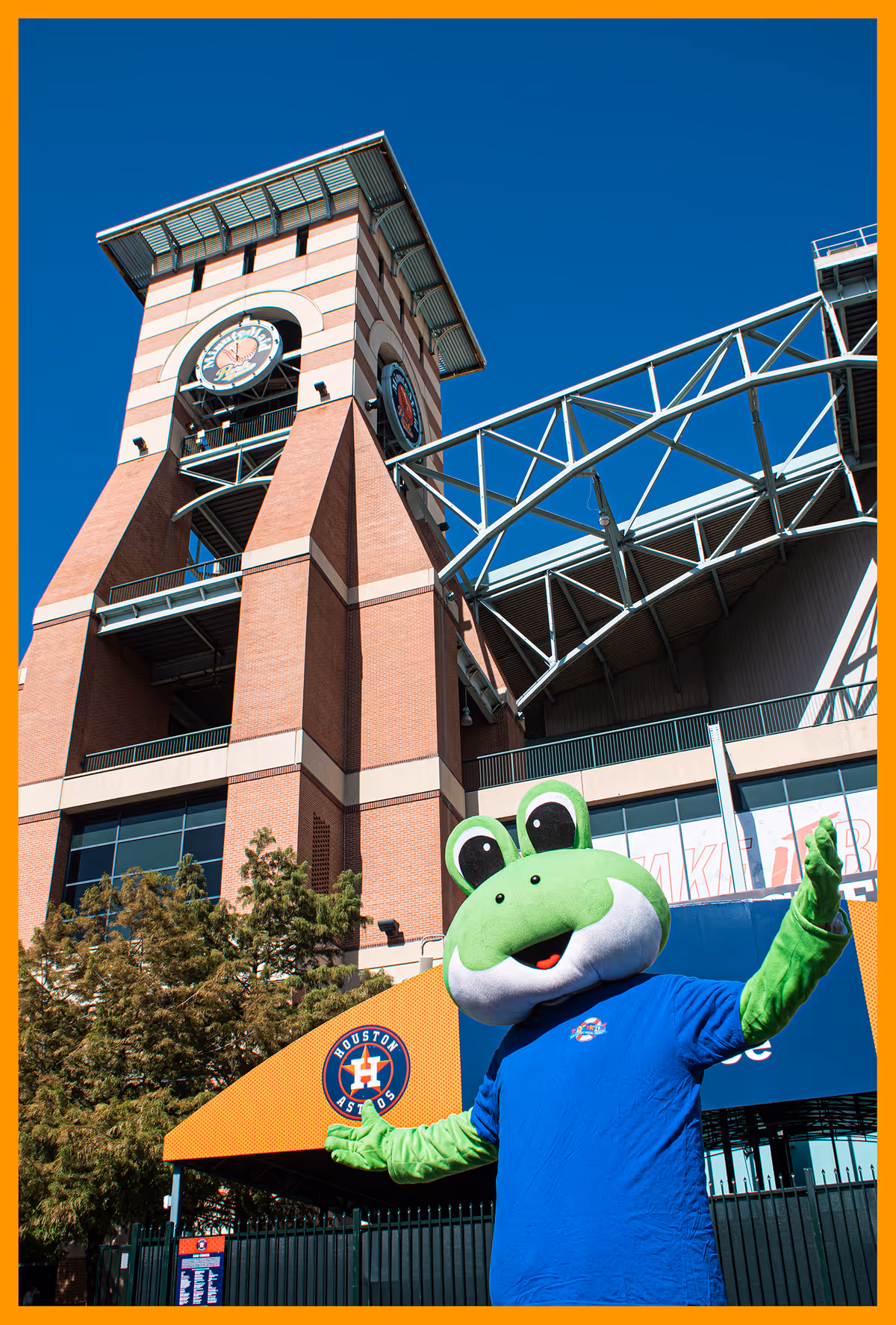 Tall brick building with clock tower and a green frog mascot outside.