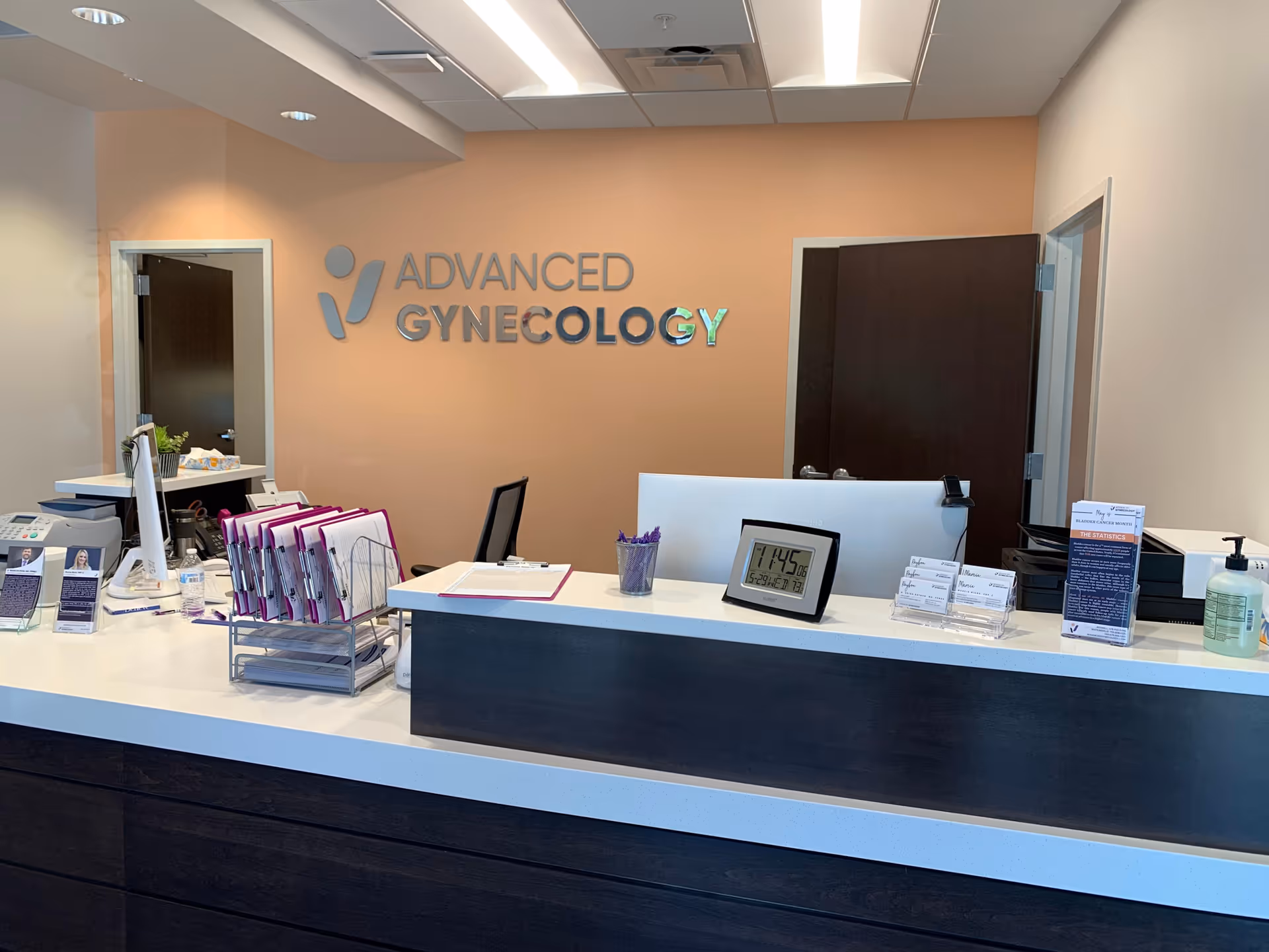 Reception desk in a medical clinic lobby with peach wall and Advanced Gynecology sign.